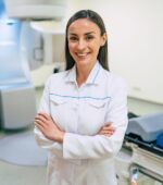 A medical imaging tech smiling in front of an imaging machine