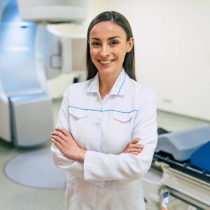 A medical imaging tech smiling in front of an imaging machine