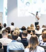 A group of people listen to a speaker making a presentation